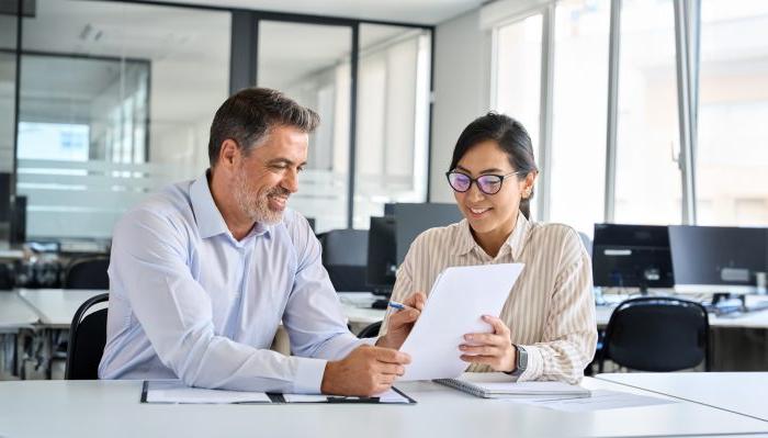 Two people at a desk look at a document together.